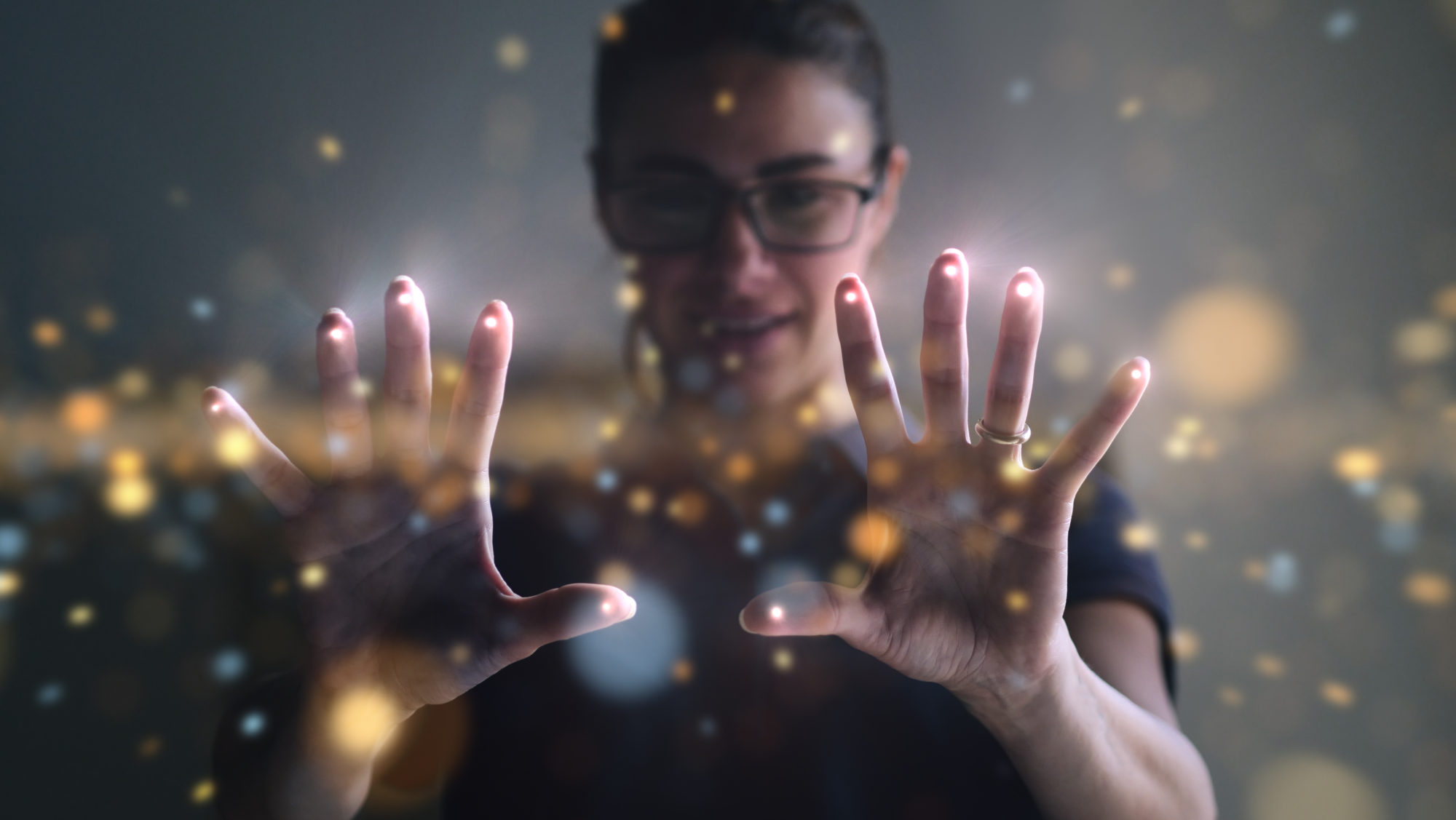 Person with glasses holding hands forward with glowing fingertips and sparkling light effects.