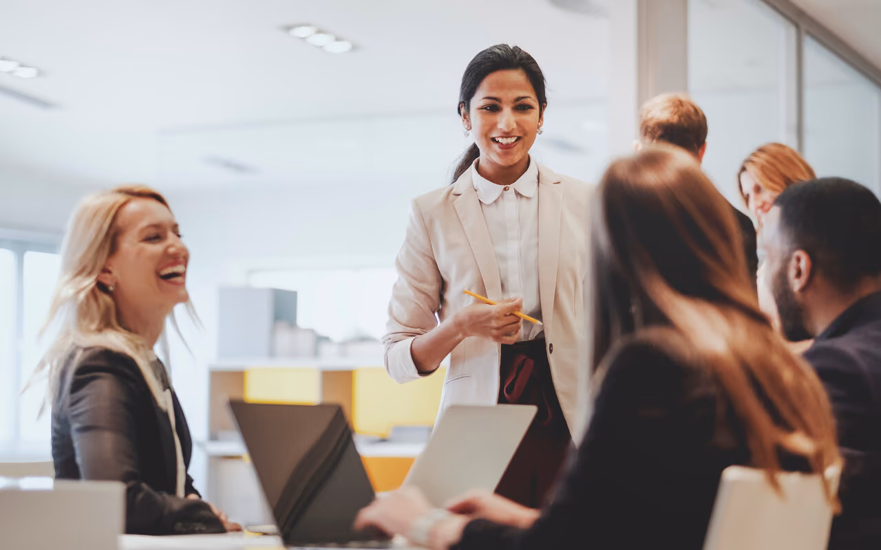 Businesswoman standing and speaking to seated colleagues in a modern office setting.