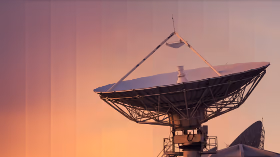 Large satellite dish antenna against a sunset sky with warm orange and purple hues.
