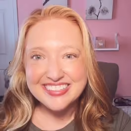 Smiling woman with long blonde hair in a room with pink walls and wall art.