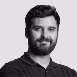 Portrait of a man with dark hair and beard wearing a black shirt against a light gray background.