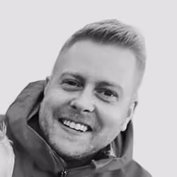 Smiling man with short hair wearing a jacket against a plain background.