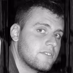 Close-up portrait of a young man with short hair and facial stubble looking sideways.