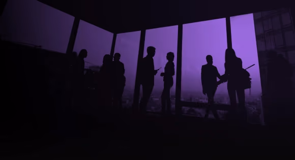 Silhouettes of people talking near large windows with a city view at dusk or dawn.
