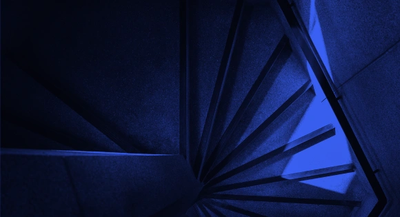 Dark blue spiral staircase viewed from above with sharp shadows and angles.