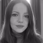 Black and white portrait of a woman with long hair wearing a ribbed turtleneck sweater, looking directly at the camera with a neutral expression against a background with curtains.