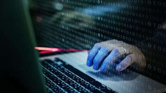Hands typing on a laptop with binary code overlaid.