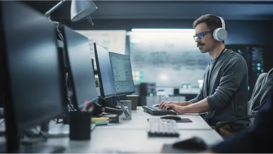 Man wearing headphones working at multiple computer monitors.