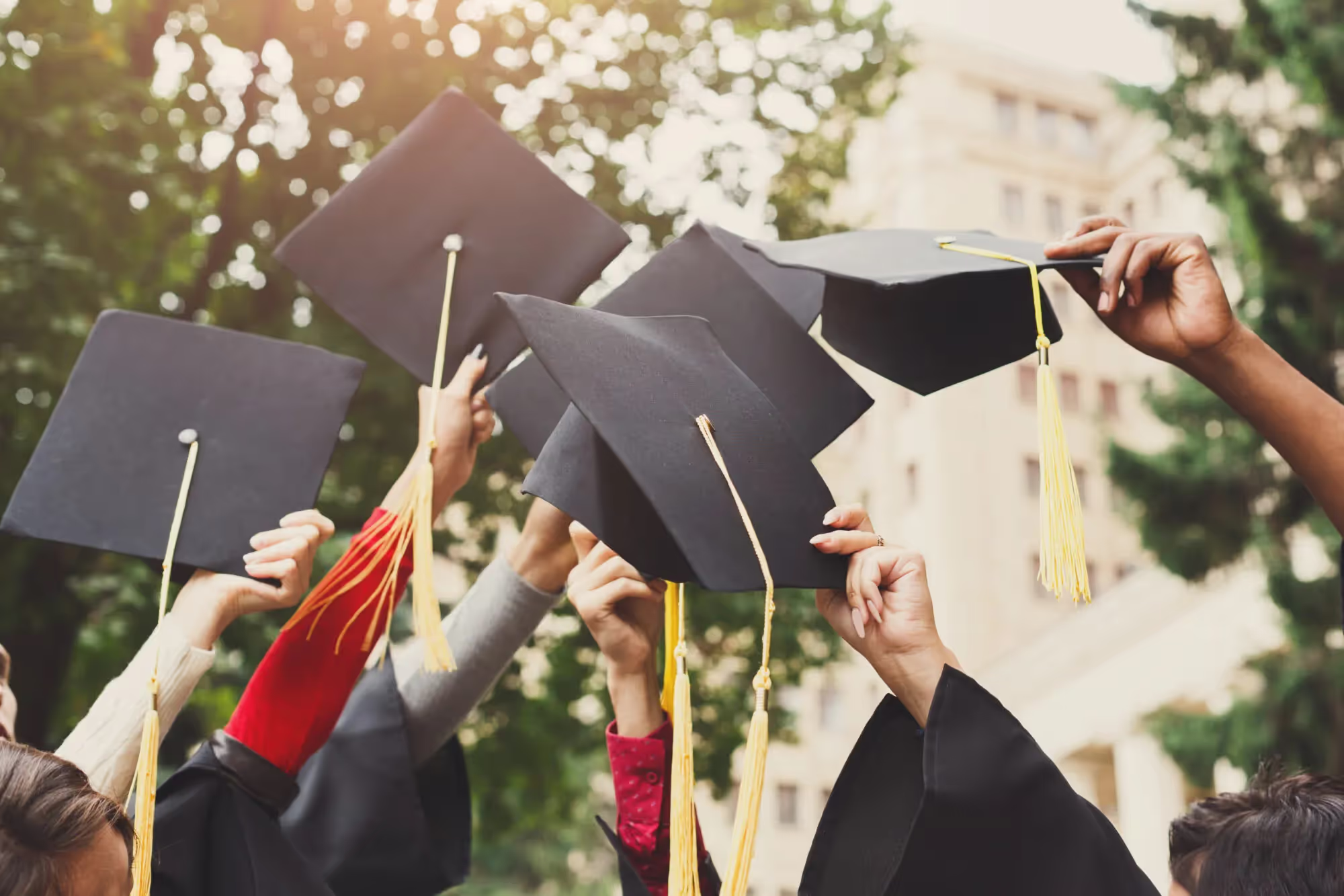Graduates raising their mortarboard caps outdoors.