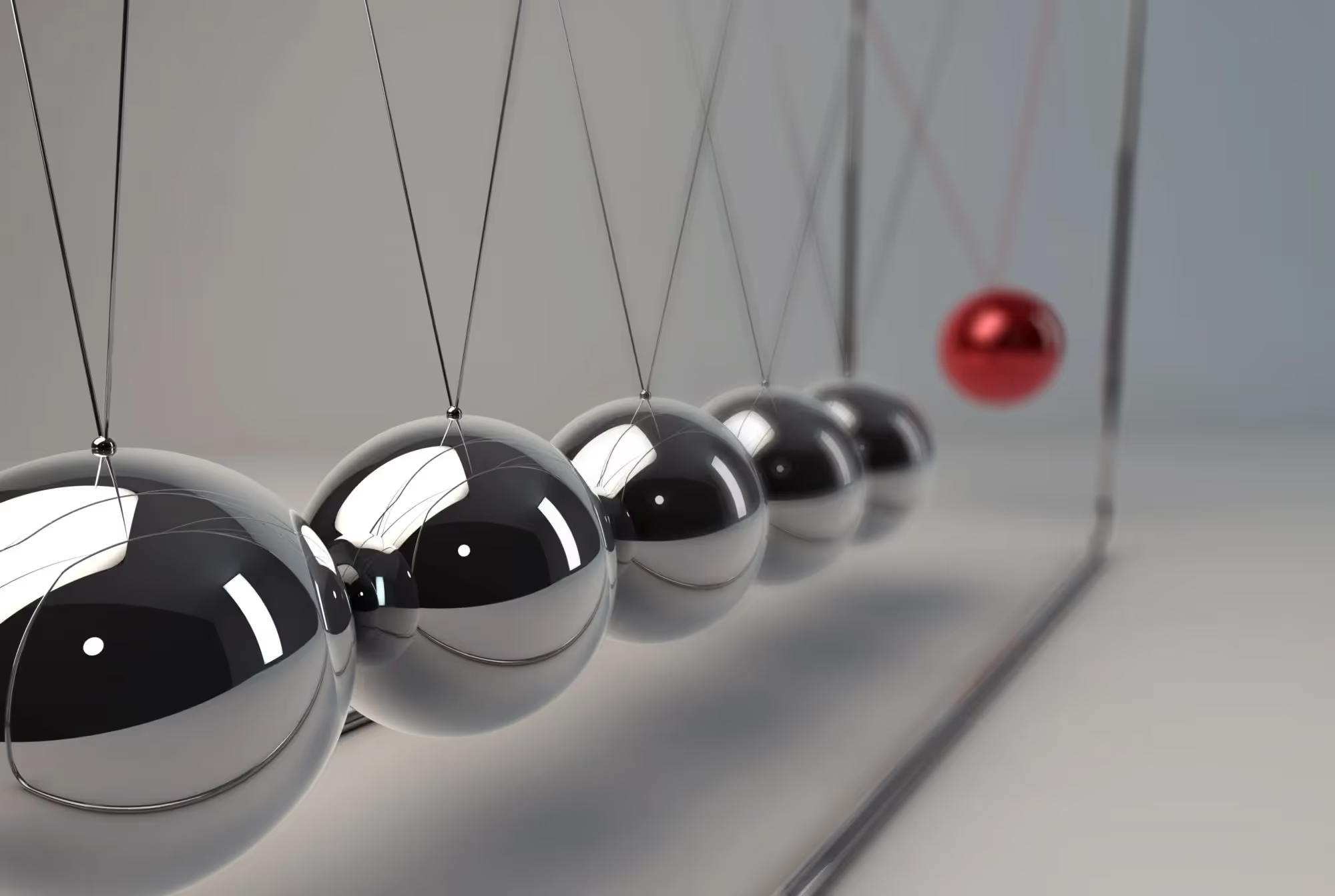 Newton's cradle with five silver balls and one red ball suspended on strings in motion.
