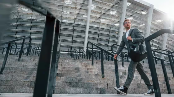 Man in a gray suit carrying a black bag walking up outdoor concrete stairs by a modern building.