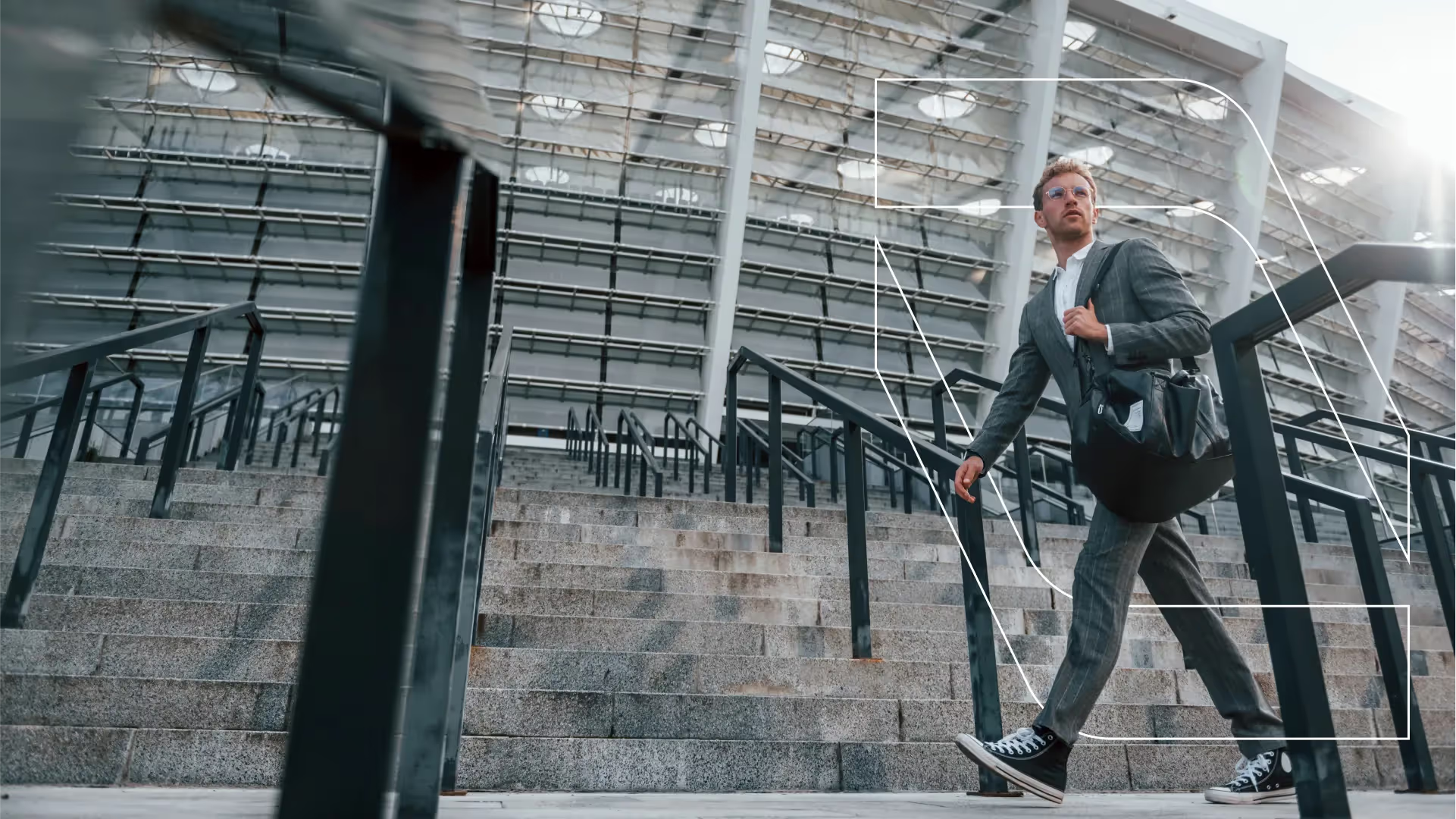 Man in a gray suit and sneakers walking up outdoor stairs near a modern glass building.
