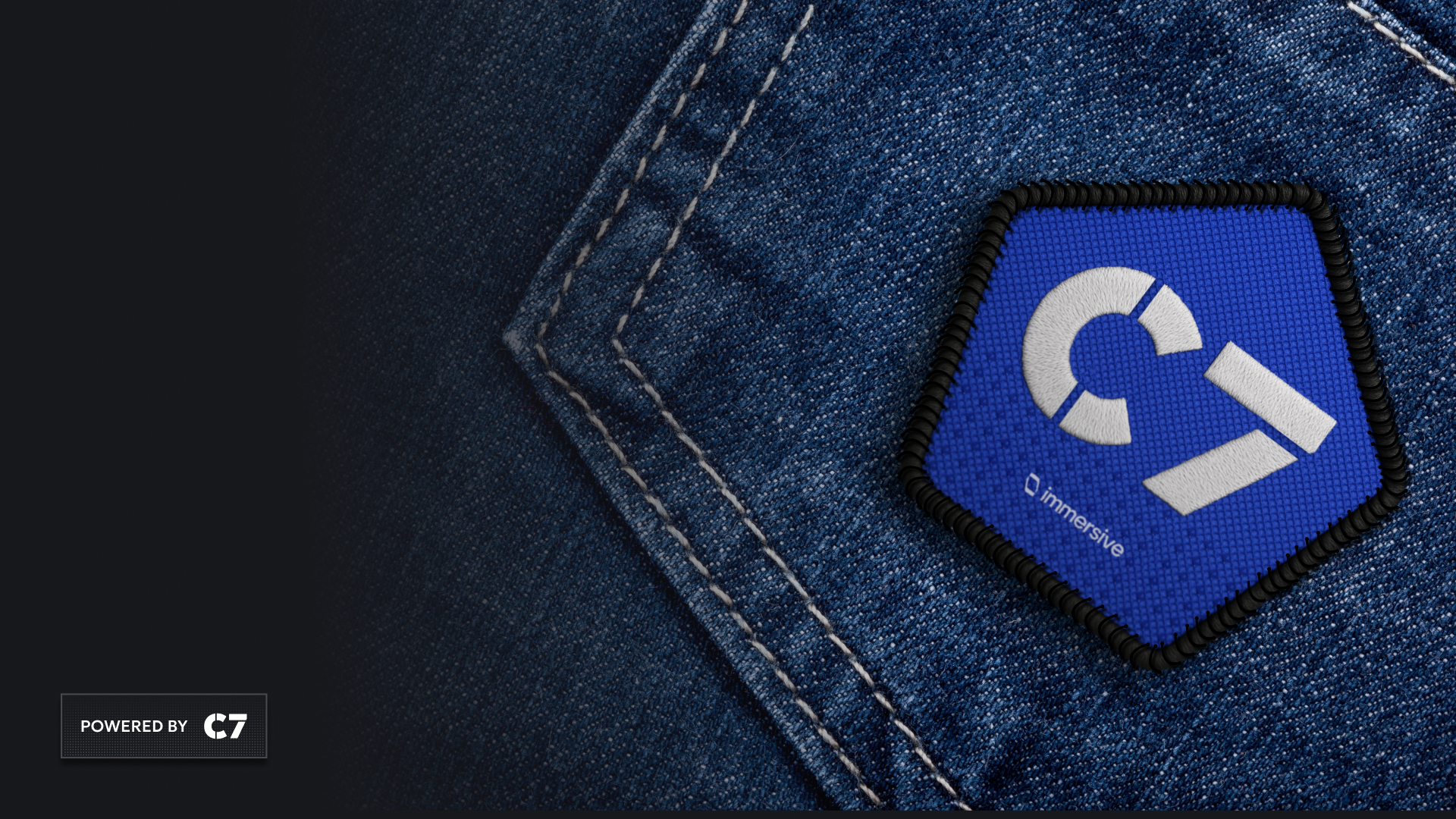 Blue pentagon patch with 'C7 Immersive' logo on denim fabric near stitched seam.