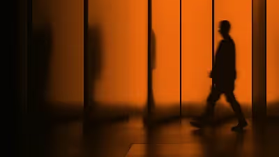 Silhouette walking past orange-lit glass panels.