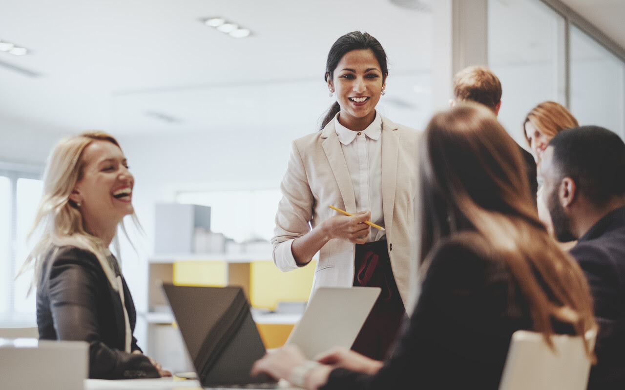 Businesswoman standing and speaking to seated colleagues in a modern office setting.