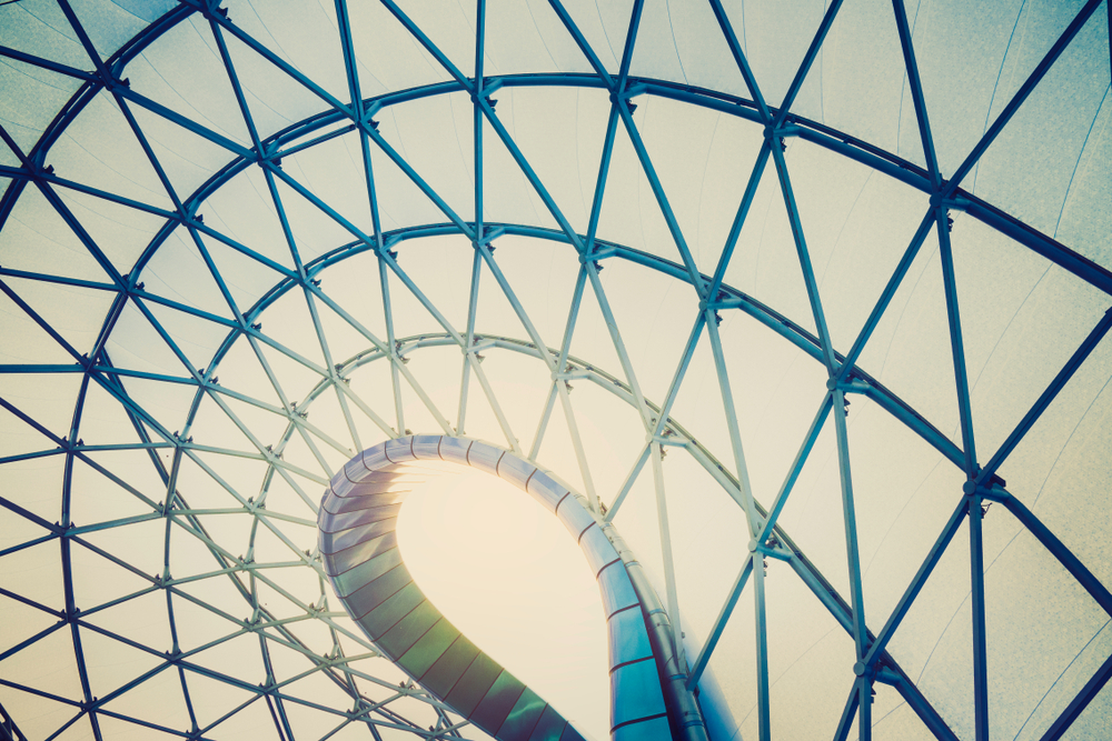 Curved metal staircase spirals upward inside a glass and steel lattice dome roof.