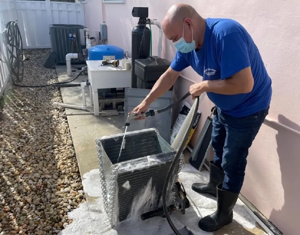 Technician cleaning condenser coils for seasonal maintenance in Miami, emphasizing preparation for summer