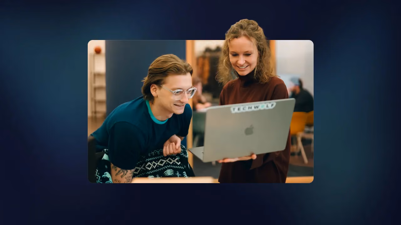 Two colleagues smiling at a laptop with a TechWolf sticker in an office