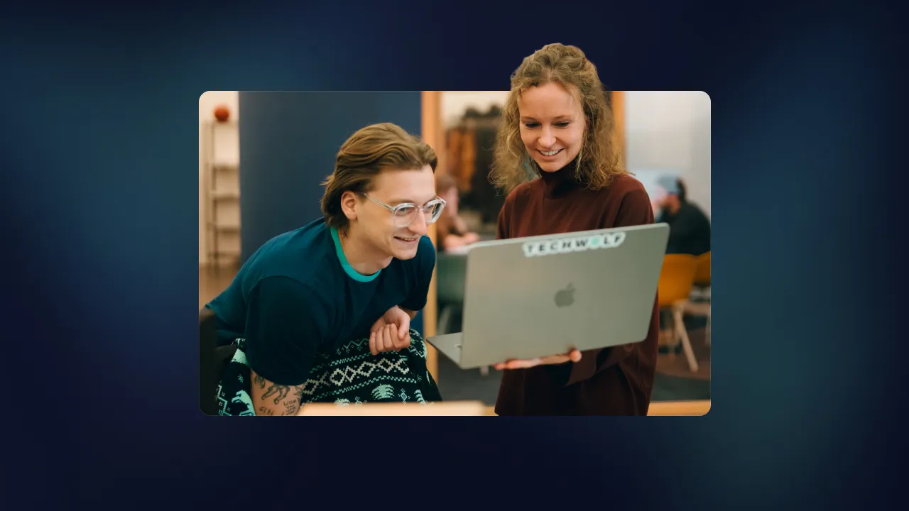 Two colleagues smiling at a laptop with a TechWolf sticker in an office
