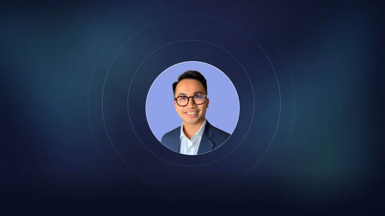 Circular headshot of a smiling man in glasses and a blazer on a lilac background