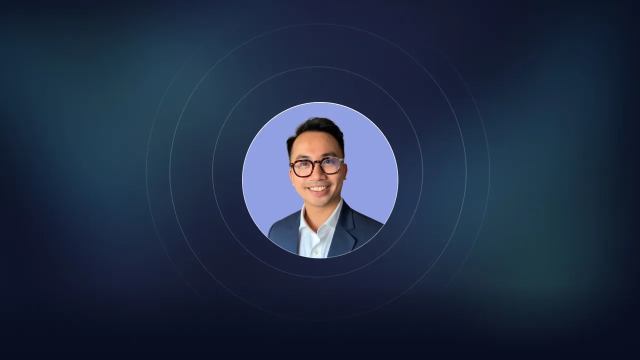 Circular headshot of a smiling man in glasses and a blazer on a lilac background