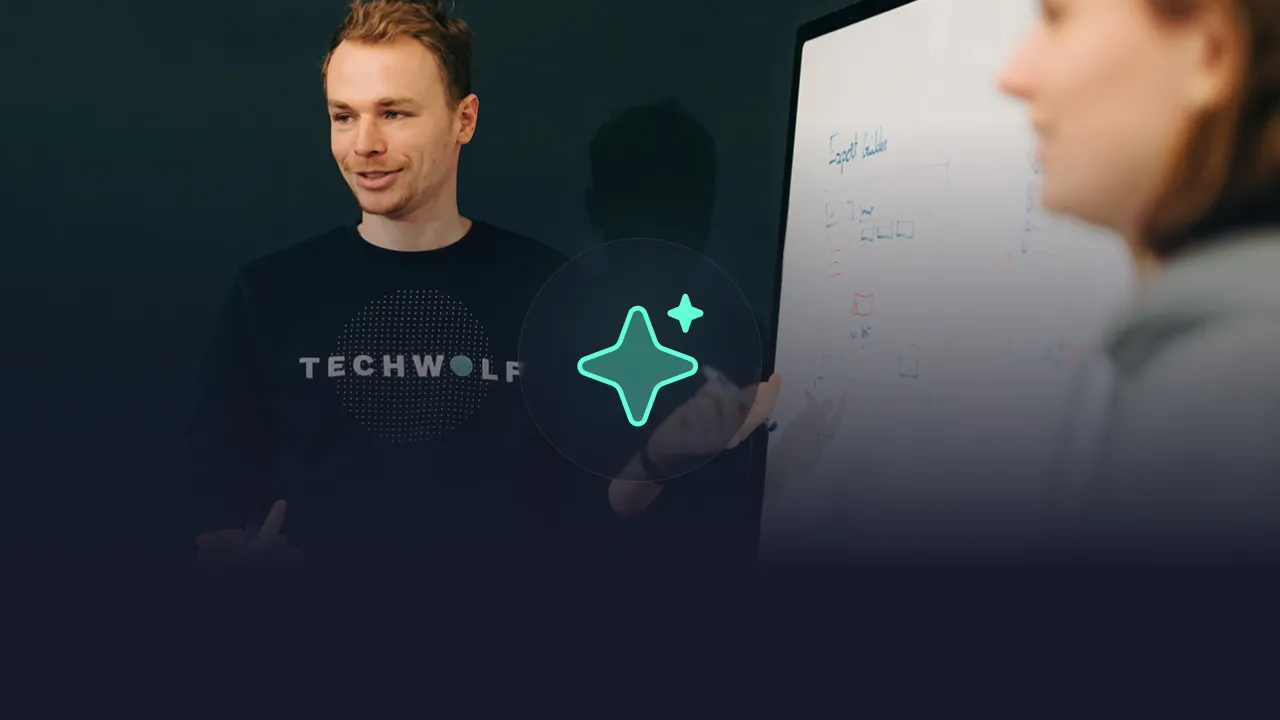 Man in a TechWolf sweater at a whiteboard with a colleague, mint AI sparkle icon overlaid
