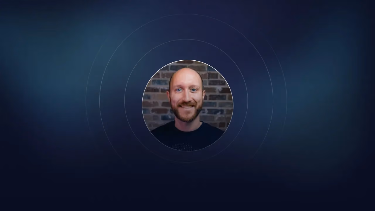 Circular portrait of a smiling bald man with a beard in front of a brick wall
