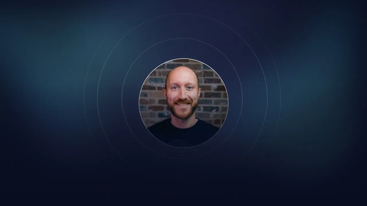 Circular portrait of a smiling bald man with a beard in front of a brick wall