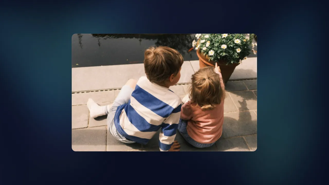 Two young children sitting on a quay by the water, pointing at a pot of daisies