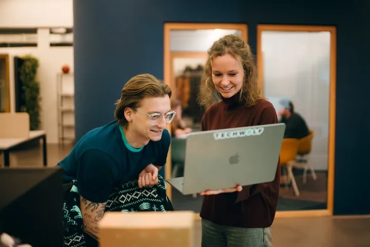 Two TechWolf colleagues smiling at a laptop with a TechWolf sticker in the office