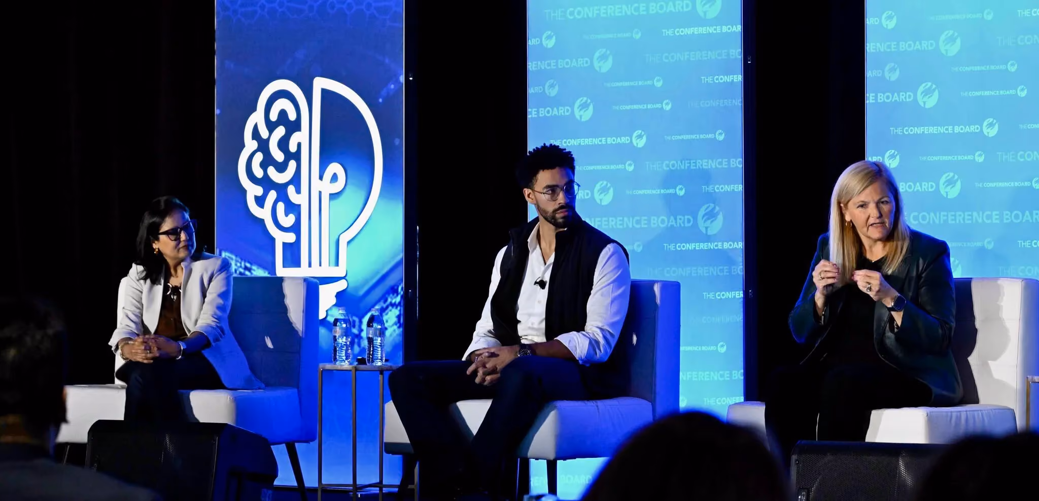 Three panellists seated on stage at a Conference Board event with branded backdrops