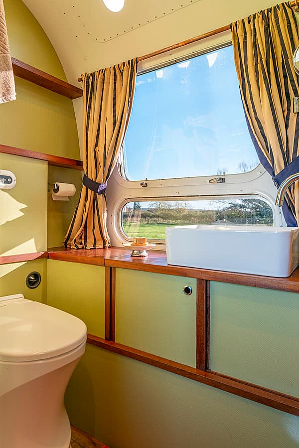 Bathroom of the Silver Dream Airstream looking out to a blue sky, shows the sink, toilet and cupboards.