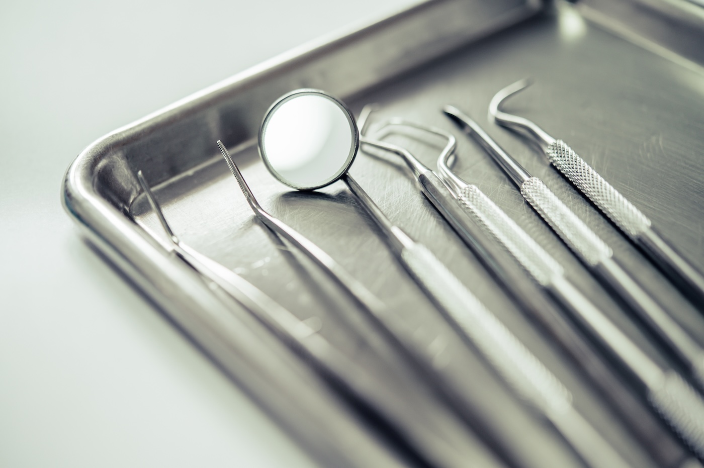Close-up of metal dental tools including mirror and probes arranged on a sterile tray.