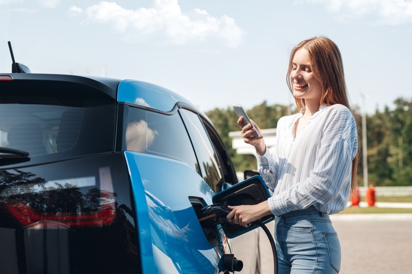 Smiling woman charging electric vehicle