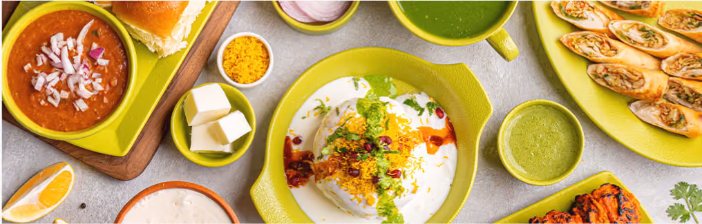 A vibrant spread of Indian street food (Chaat), including Dahi Bhalla and Pav Bhaji.