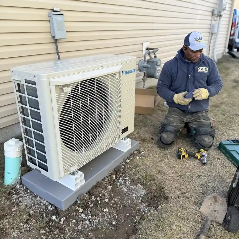 Technician kneeling beside a Daikin outdoor air conditioning unit, surrounded by tools and equipment for installation or maintenance.