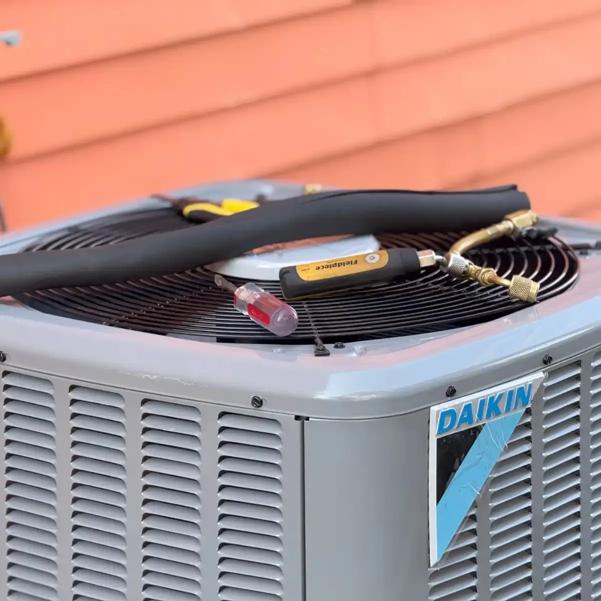 A Daikin air conditioning unit with service tools, including a screwdriver and gauge, on top.