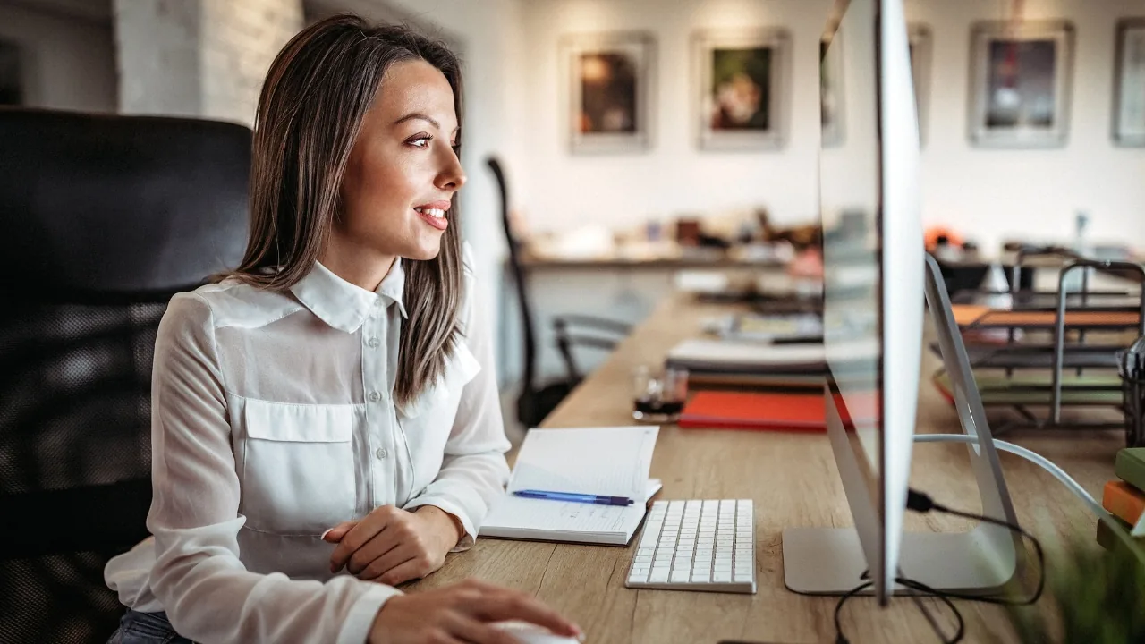 Femme assise à son poste de travail, regardant un écran dans un bureau moderne