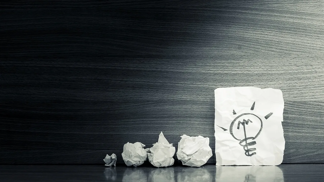 Croquis d’ampoule sur une feuille avec des boules de papier froissé, symbole d’idée