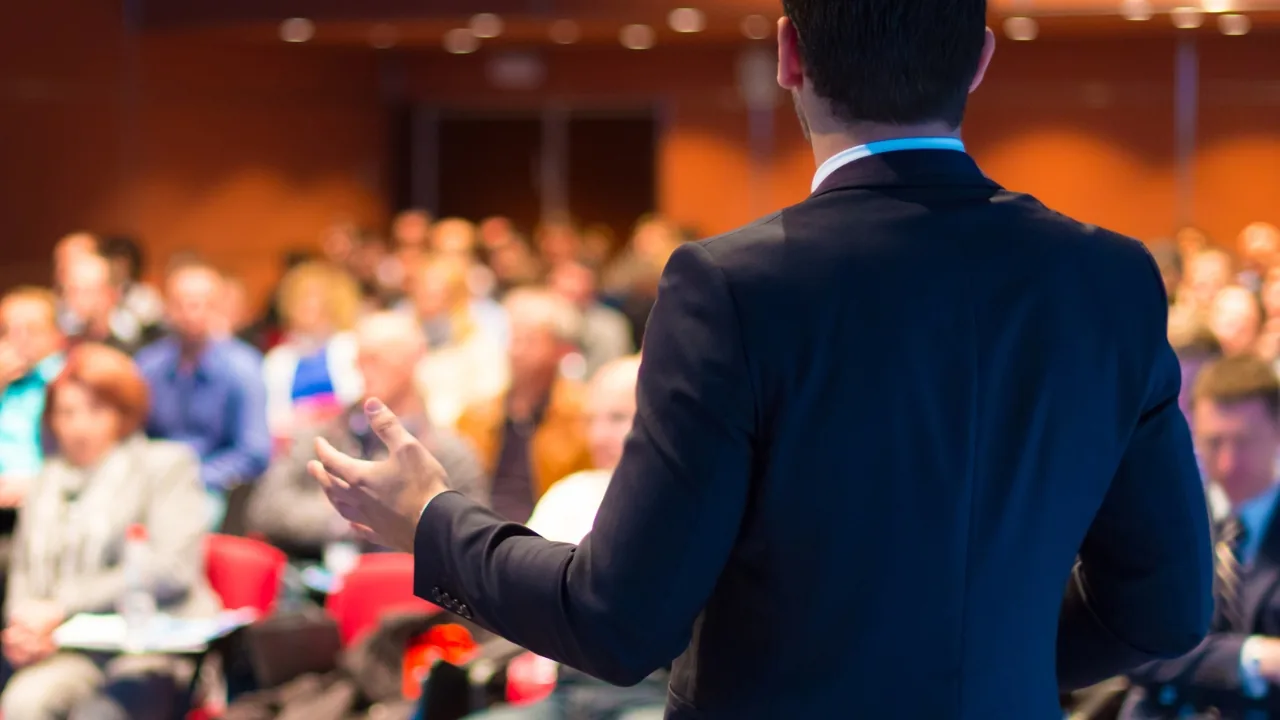 Intervenant sur scène face à un public lors d’une conférence professionnelle