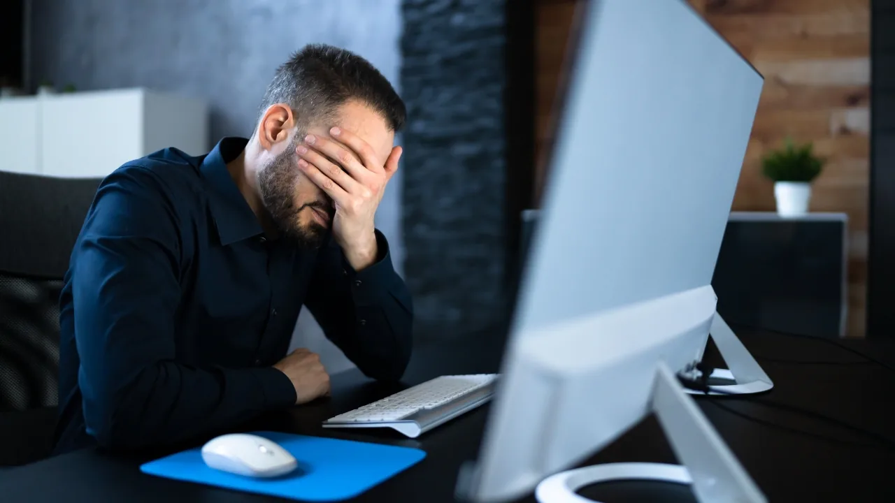 Homme stressé à son bureau, la tête dans la main devant un ordinateur