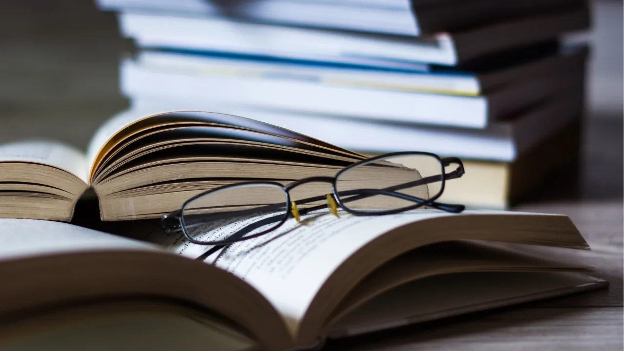 Livre ouvert avec des lunettes posées dessus, à côté d’une pile de livres