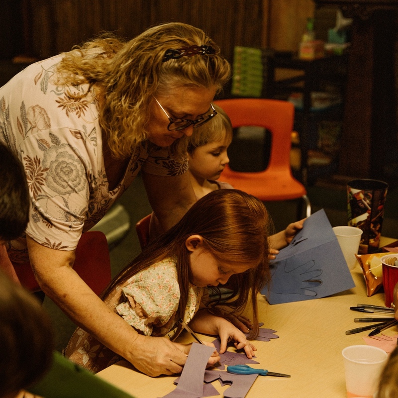 An adult volunteer helps a child with a craft.