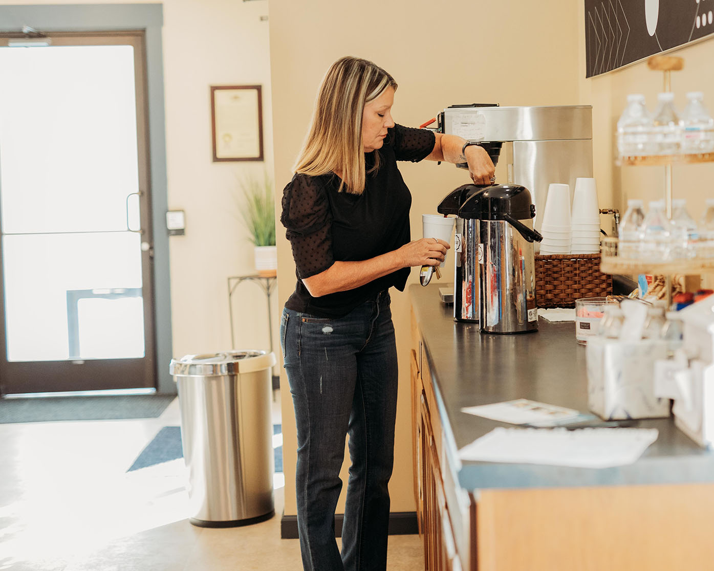 A woman fills up a cup of coffee from a carafe.
