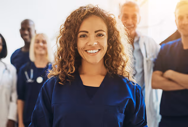 A physician in scrubs standing with other physicians.