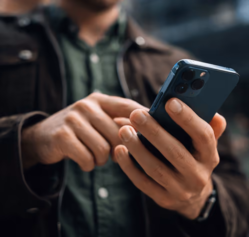 Person using a smartphone with a dark green shirt and brown jacket outdoors.