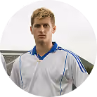 Young man with short blond hair wearing a white sports jersey with blue trim.