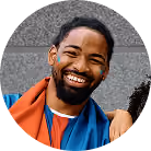 Smiling bearded man with earbuds wearing a blue jacket and red inner shirt