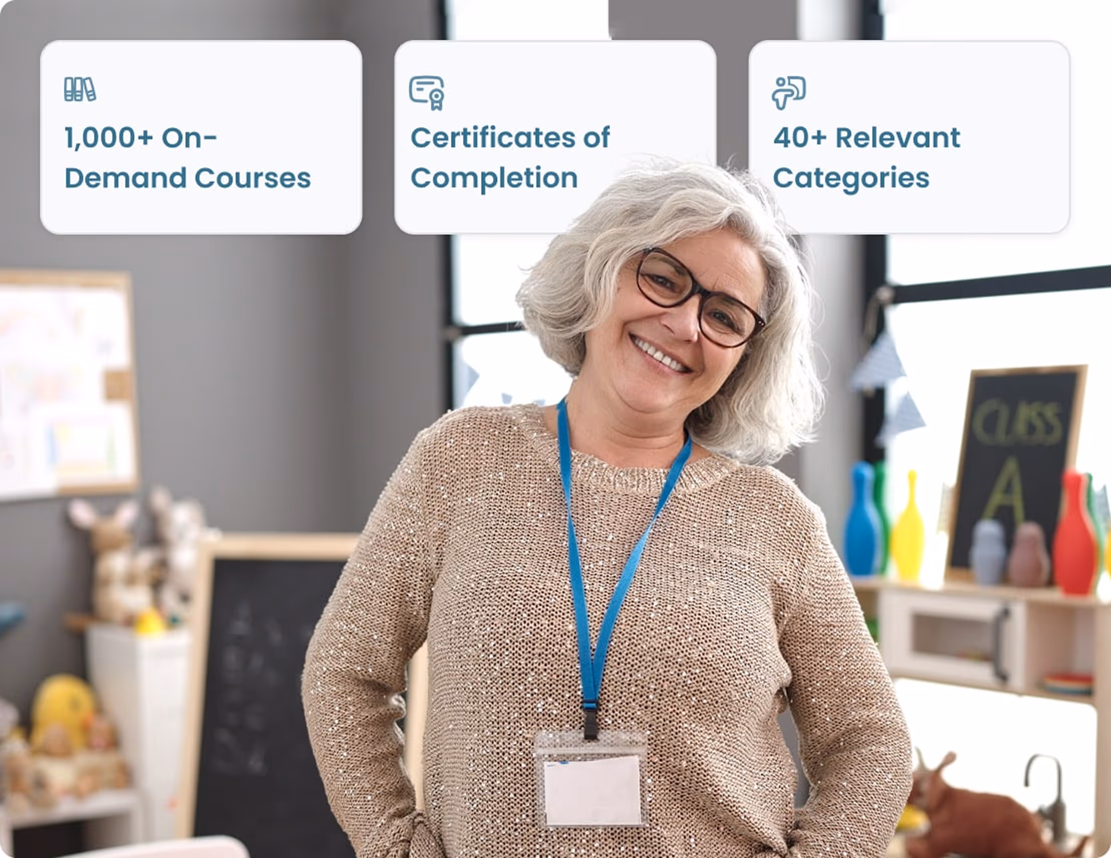 Smiling middle-aged woman with gray hair and glasses wearing a badge, standing in a colorful classroom with educational toys and a chalkboard.