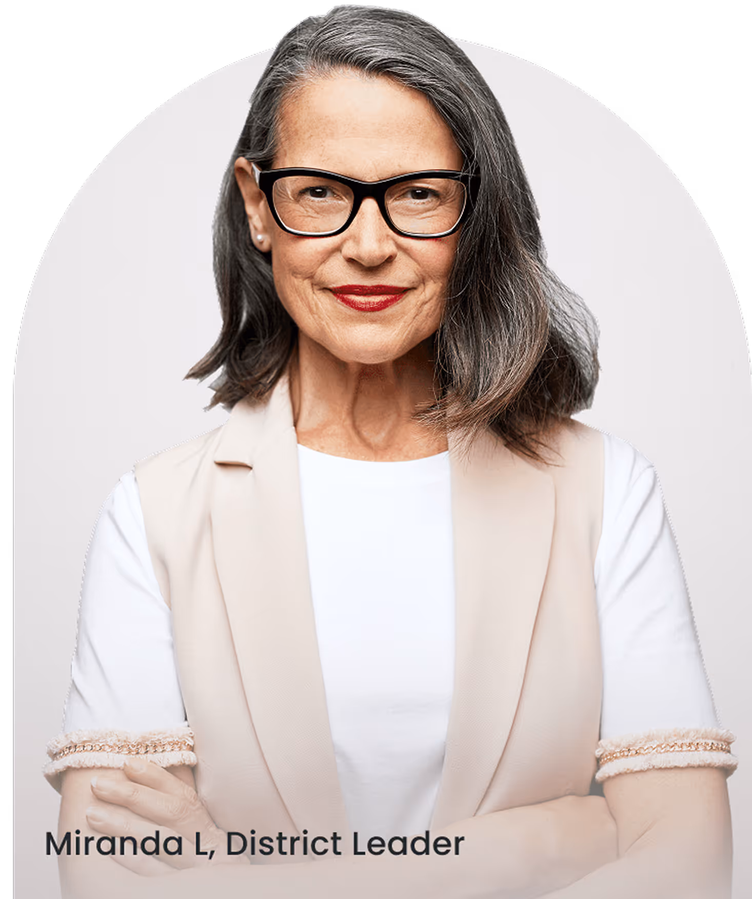 Confident middle-aged woman with gray hair and glasses wearing a beige vest and white shirt, arms crossed.